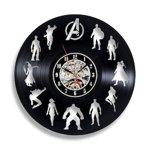 Pode incluir: Um relógio de vinil preto com uma silhueta prateada dos personagens dos Vingadores, incluindo Homem de Ferro, Capitão América, Thor, Hulk, Viúva Negra, Gavião Arqueiro, e mais. O mostrador do relógio tem um mecanismo de relógio prateado com números e ponteiros pretos.