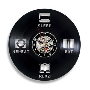 May include: Black vinyl record clock with a silver clock face and silver hands. The clock face has numbers 1-12 and the words "SLEEP", "REPEAT", "EAT", and "READ" around the clock face.