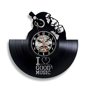 May include: A black vinyl record clock with a silhouette of a person wearing headphones and holding a microphone. The clock face has Roman numerals and the words "I Love Good Music" are printed below the clock face.