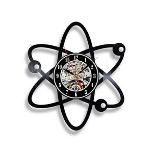 May include: Black vinyl record clock shaped like an atom with a silver clock face and black hands. The clock face has numbers 1 through 12.
