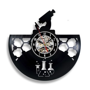 Könnte beinhalten: Schwarze Schallplattenuhr mit einem Mikroskop- und Becherdesign. Das Zifferblatt der Uhr hat einen silbernen Rand und schwarze Zahlen. Die Zeiger der Uhr sind rot und schwarz.