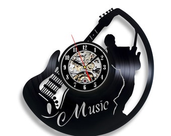 Könnte beinhalten: Schwarze Schallplattenuhr mit einer Silhouette eines Gitarristen, der eine E-Gitarre spielt. Das Zifferblatt der Uhr befindet sich in der Mitte der Schallplatte und hat ein silbernes und schwarzes Uhrwerk. Die Worte "Musik" sind in einer kursivschriftlichen Schriftart am unteren Rand der Schallplatte geschrieben.