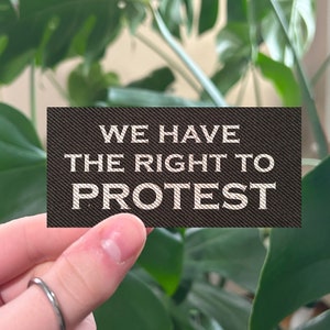 May include: A black fabric patch with white text that reads "We have the right to protest."