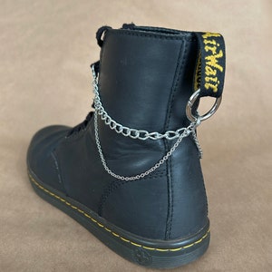 May include: Black leather ankle boots with a silver chain attached to the top of the boot. The boot has a yellow "AirWair" tag on the side.