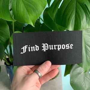 May include: Black fabric patch with white text that reads "Find Purpose" in a gothic font.