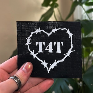 May include: White iron-on patch with a barbed wire heart design and the text "T4T" on a black background.