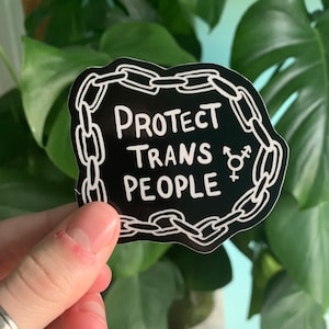 May include: Black and white sticker with a chain border and the text "PROTECT TRANS PEOPLE" with a transgender symbol.
