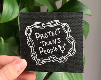 May include: Black fabric patch with white text and a chain border. The text reads "Protect Trans People" with a transgender symbol.
