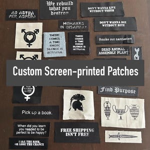 May include: A collection of black and white screen-printed patches with various designs and slogans. Some of the patches feature text such as "We rebuild what you destroy", "Mohawks in Disarray", "There comes a time where silence is betrayal", "Don't wanna live without teeth", "Don't wanna die without bite", "Smoke out narcissism", "Dead animal assembly plant", "Find purpose", "Pick up a book", "When did you learn you needed to be perfect to be happy?", "Take the risk, or lose the chance", and "Free shipping isn't free".