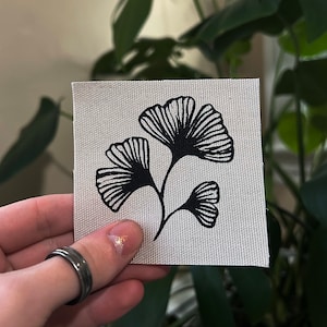May include: Black and white illustration of three ginkgo leaves on a white fabric background.