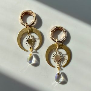 May include: Gold tone earrings with a crescent moon design, a sun charm, and a teardrop-shaped crystal pendant.