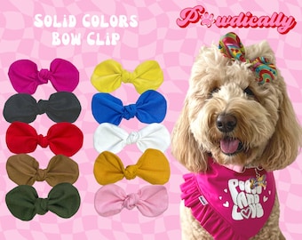 May include: A collection of solid-colored bow clips in various colors, including pink, black, red, and yellow. The text "SOLID COLORS BOW CLIP" is displayed above the bows. A dog is wearing a matching bow and bandana with the words "Peace and Love".