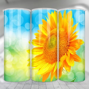 May include: A tumbler with a design of a bright yellow sunflower with a green background and a blue sky with white bokeh circles.