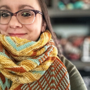 Puede incluir: Una mujer con gafas y una bufanda de punto con un patrón geométrico en tonos naranja, amarillo y verde. La bufanda está drapeada alrededor de su cuello y hombros.
