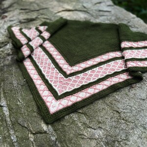 May include: A green knitted shawl with a pink and white border. The shawl is folded and lying on a rock.