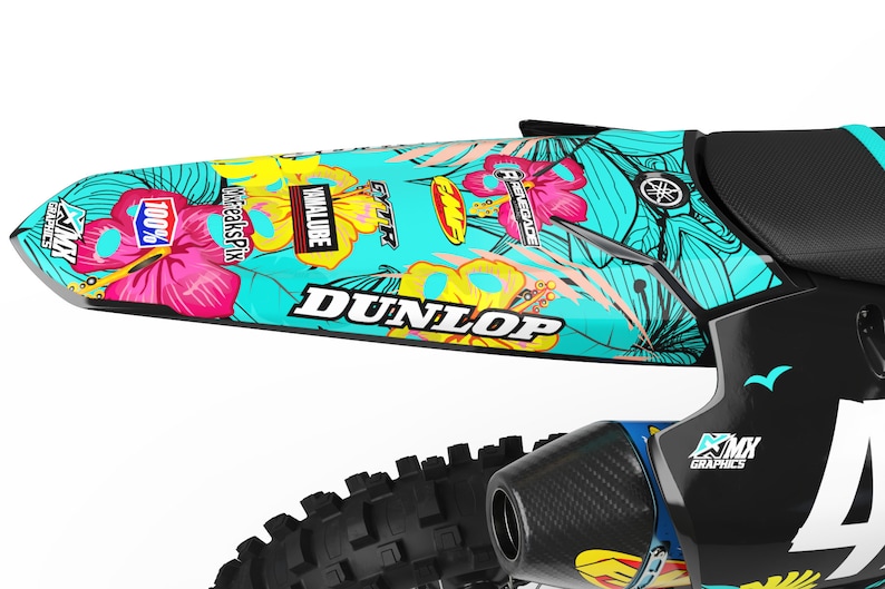 May include: A turquoise and black dirt bike with floral graphics. The graphics feature pink hibiscus flowers, yellow and white leaves, and the words "Dunlop", "VMXALUBE", "FREAKSPIX", "100%", and "RENEGADE".