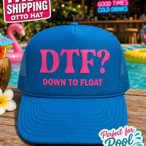 May include: A bright blue trucker hat featuring a mesh back and a structured front panel. The text DTF? DOWN TO FLOAT is printed in bold pink lettering across the center of the front panel. The hat includes a matching blue rope trim detail.