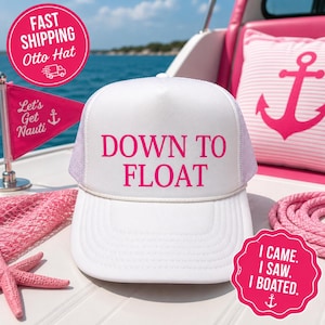 Könnte beinhalten: Eine weiße Trucker-Cap mit Netzrückseite und weißem Schirm. Auf der Vorderseite steht der Text DOWN TO FLOAT in kräftigen, pinkfarbenen Buchstaben. Eine dünne weiße Kordel verläuft horizontal über der Basis der Vorderseite.