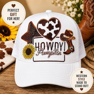 Puede incluir: Gorra de camionero blanca con parte trasera de malla y visera curva. La gorra presenta parches que incluyen un corazón marrón con estampado de vaca, una estrella, un girasol y una bota de vaquero. El texto "HOWDY Pumpkin" está bordado en la parte delantera.