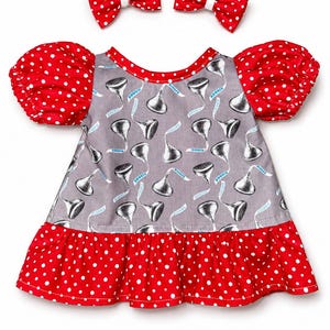 May include: A gray dress with a pattern of Hershey's Kisses, red polka dot sleeves, and a red polka dot ruffle. Two red polka dot bows are also included.