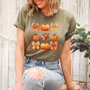 May include: A green t-shirt with a pattern of orange pumpkins, brown footballs, and orange and white gingham bows.