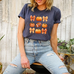 May include: A navy blue t-shirt with a graphic of pumpkins, footballs, and gingham bows.