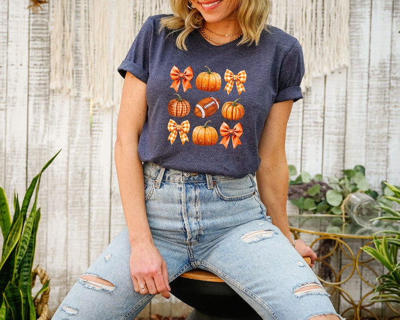 May include: A navy blue t-shirt with a graphic of pumpkins, footballs, and gingham bows.
