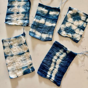 Könnte beinhalten: Fünf kleine, rechteckige Stoffstücke mit einem Batikmuster in Blau- und Weißtönen. Jedes Stück hat an einer Ecke eine Schnur befestigt. Der Stoff scheint zerknittert zu sein, wobei die Farbe einen Marmoreffekt erzeugt.
