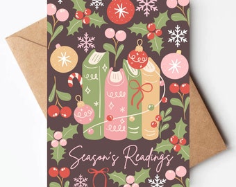 May include: A Christmas card with a dark brown background featuring a stack of four books decorated with holly, ornaments, and snowflakes. The text "Season's Readings" is written in pink and green lettering.