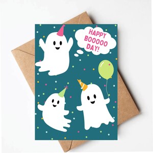May include: A teal blue card with three white ghosts wearing party hats. The ghosts have happy faces and one is holding a green balloon. The card says "Happy Boooooo Day!" in a white speech bubble.