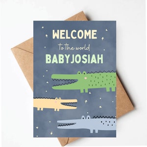 May include: A blue card with the text "WELCOME to the world BABY JOSIAH" and three cartoon alligators in green, yellow, and blue. The card has a white background with white stars.