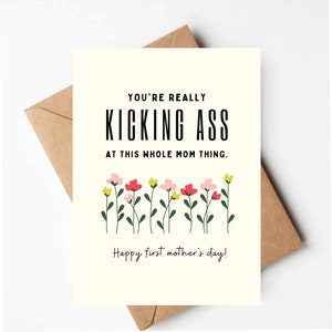 May include: A greeting card with the text "YOU'RE REALLY KICKING ASS AT THIS WHOLE MOM THING." and "Happy first mother's day!" in black font. The card features a floral design with pink, red, and yellow flowers. The card is on a brown envelope.