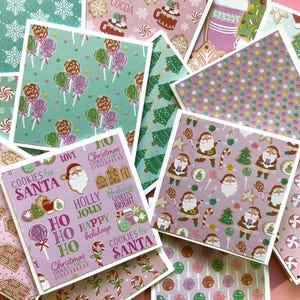 May include: A stack of Christmas-themed greeting cards with various designs featuring candy canes, gingerbread houses, and Santa Claus. The cards are printed on pink and green paper with white borders.