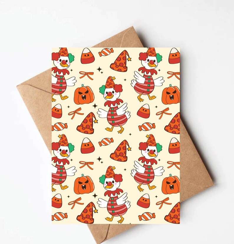 May include: A greeting card with a repeating pattern of a clown duck, pumpkins, candy corn, and party hats on a cream background. The clown duck is wearing a red and white striped shirt and a clown hat. The card is placed on a brown envelope.