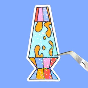 Puede incluir: Una pegatina holográfica de una lámpara de lava con una base azul, lava naranja y una base rosa y roja.