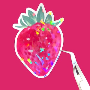 May include: A holographic sticker of a red strawberry with green leaves. The sticker is on a pink background and is being held by a pair of tweezers.