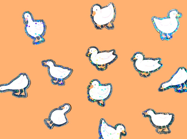 May include: A set of 11 iridescent holographic stickers featuring white ducks in various poses. The stickers are on a light orange background.
