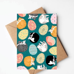 May include: A teal blue card with a repeating pattern of cats sleeping inside colorful Easter eggs. The cats are orange, black and white, and gray. The eggs are decorated with floral and geometric designs.