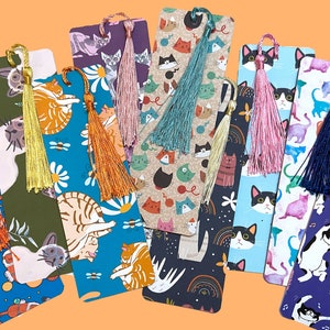 May include: A set of ten colorful bookmarks featuring cats and tassels. The bookmarks are made of cardstock and have a variety of designs, including cats playing music, cats with flowers, and cats with yarn. The tassels are made of different colors of yarn.