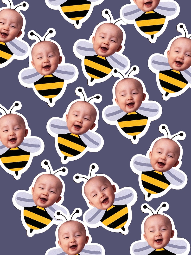 May include: A repeating pattern of smiling baby faces superimposed on cartoon bee bodies. The bees have black and yellow striped bodies, white wings, and antennae. The background is a solid, muted purple.