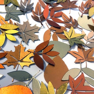 May include: Assortment of fall leaves in various shades of brown, gold, and green. The leaves are cut from paper and have a metallic sheen.