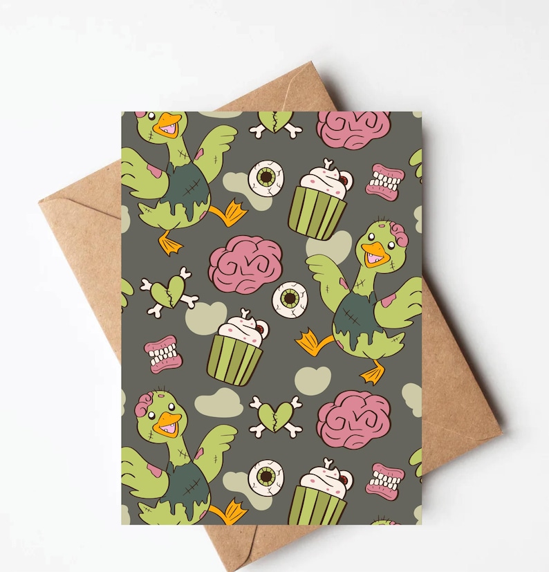 May include: Greeting card with a repeating pattern of zombie ducks, cupcakes, eyeballs, brains, and broken hearts on a gray background. The card is paired with a brown envelope, perfect for Halloween or spooky occasions.