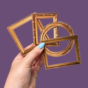 May include: A collection of three small, ornate gold-colored picture frames. The set includes one rectangular frame, one square frame, and one circular frame, all featuring detailed embossed patterns along their edges and borders.