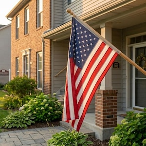 May include: A United States flag mounted on a wooden pole attached to a red brick wall of a residential building. The flag features the traditional red, white, and blue colours with stars and stripes, hanging diagonally over a porch entrance.