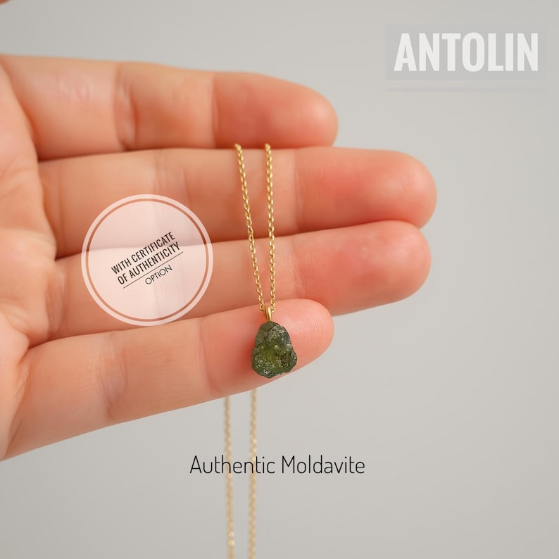 May include: A gold chain necklace featuring a small, raw, dark green moldavite pendant. The image includes the text ANTOLIN, Authentic Moldavite, and a circular badge stating WITH CERTIFICATE OF AUTHENTICITY OPTION.