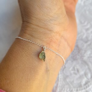 K&ouml;nnte beinhalten: Ein silbernes Kettenarmband mit einem kleinen, rohen, gr&uuml;nen Edelstein-Anh&auml;nger.