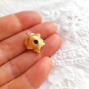 以下が含まれることがあります： 金色のペンダントで、花の模様が施されています。ペンダントは、詳細で質感のある表面と、中央に小さな穴があります。ペンダントはおそらく金属製で、ジュエリーとして着用するように設計されています。