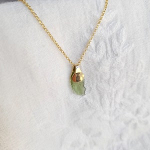 May include: A gold chain necklace with a green crystal pendant. The crystal is a raw, natural shape and is set in a gold bezel.