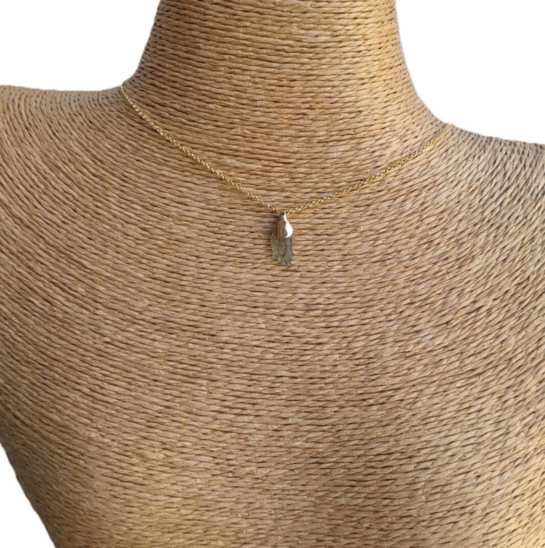 May include: A gold chain necklace with a small, green, raw crystal pendant.