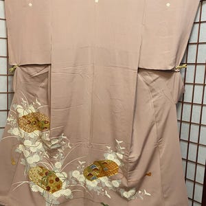 May include: A pale pink kimono with a floral pattern. The flowers are white and the leaves are green. The kimono has a gold and brown design on the bottom.